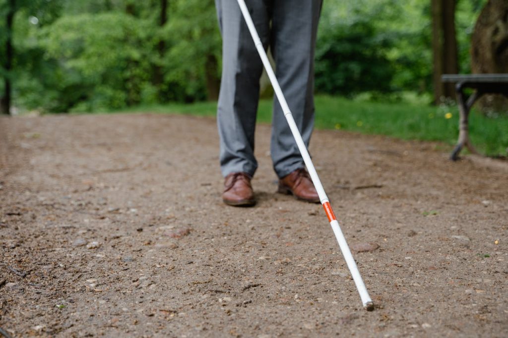 a-person-in-gray-pants-and-brown-leather-shoes-walking-while-holding-a-walking-stick-8327460 An individual with a white cane walking on a path, symbolizing independence and mobility.