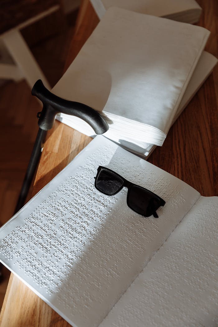Braille book open with cane and sunglasses illustrating accessibility for the visually impaired.