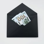 Hundred dollar bills partially visible in an open black envelope on a white background.